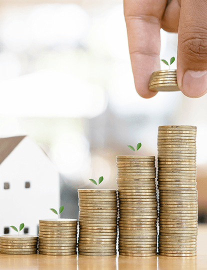 Una casa miniatura y una mano poniendo monedas en columnas Una casa miniatura y una mano poniendo monedas en columnas