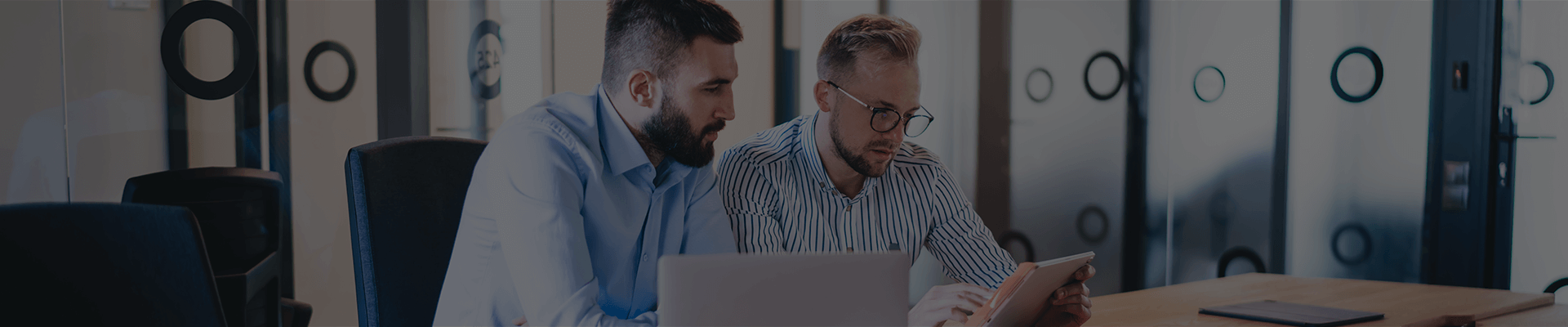 Dos hombres sentados en sala de juntas mirando un computador portátil